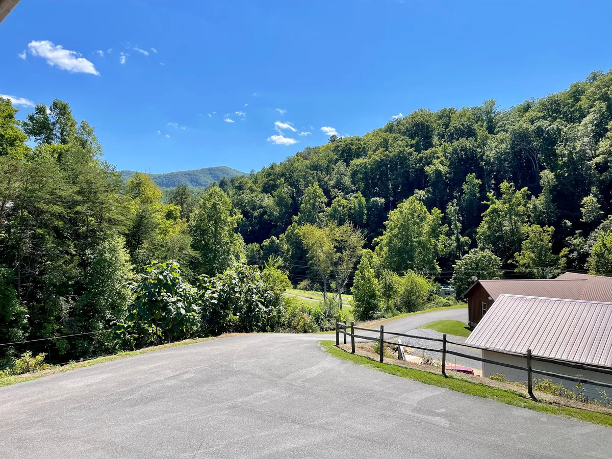 Expansive ranch grounds featuring rolling hills, lush greenery, a blue sky, roadway, and fences in the distance. The open landscape underscores the rural setting and opportunities for exploration, riding, or simply enjoying nature.