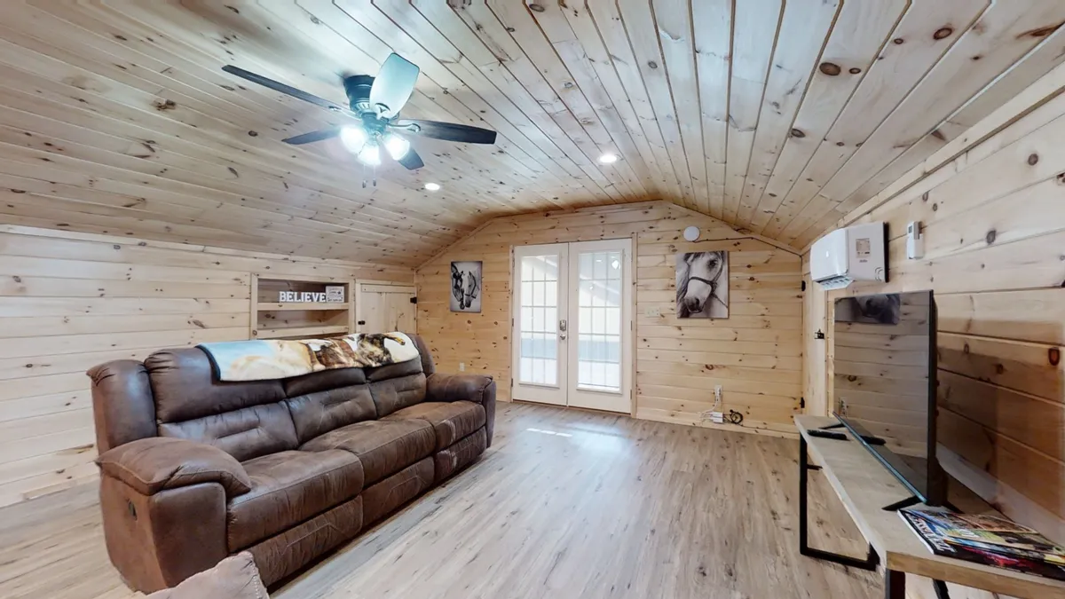 A comfortable living area featuring a plush sofa, French doors that open to the outdoors, a flat-screen TV, and tasteful artwork. The room is bathed in natural light, emphasizing its airy, inviting feel and the flow between interior and exterior spaces.
