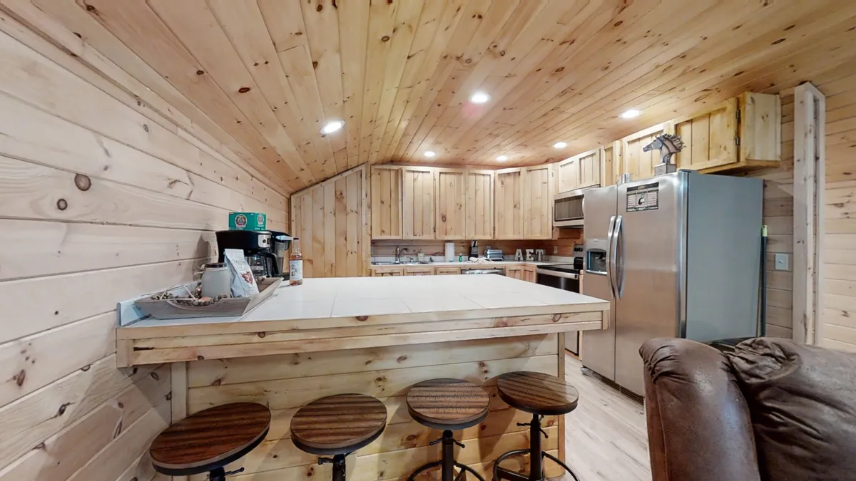 A kitchen with a wooden bar counter and stools, complemented by cabinetry and appliances in the background. The seating arrangement encourages conversation and togetherness, providing a perfect spot for relaxed meals or planning the day ahead.
