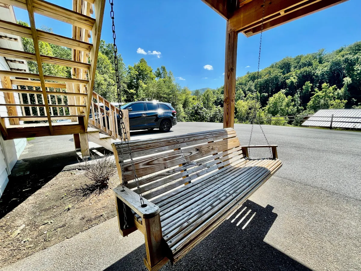 A serene exterior scene featuring a wooden swing set under the shade of lush green trees, set against a bright blue sky. The swing is positioned to provide a peaceful spot for relaxation, with open views of the ranch and a sense of spaciousness and seclusion.