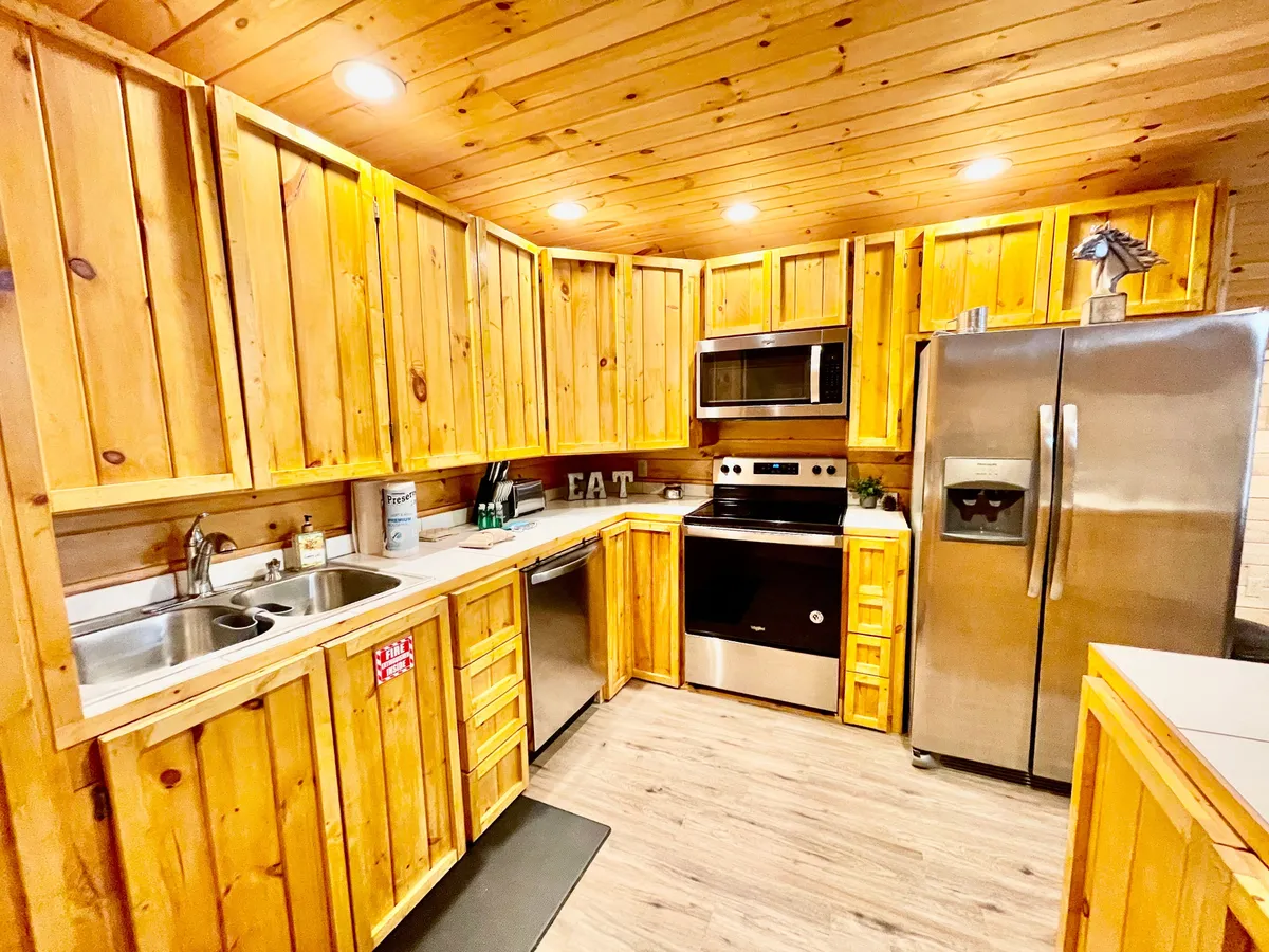 A warmly lit kitchen featuring wooden cabinetry, sleek stainless steel appliances, and inviting countertop decor. The space feels both modern and rustic, blending country charm with up-to-date functionality. The layout suggests ample room for cooking and socializing, with every essential appliance within easy reach.