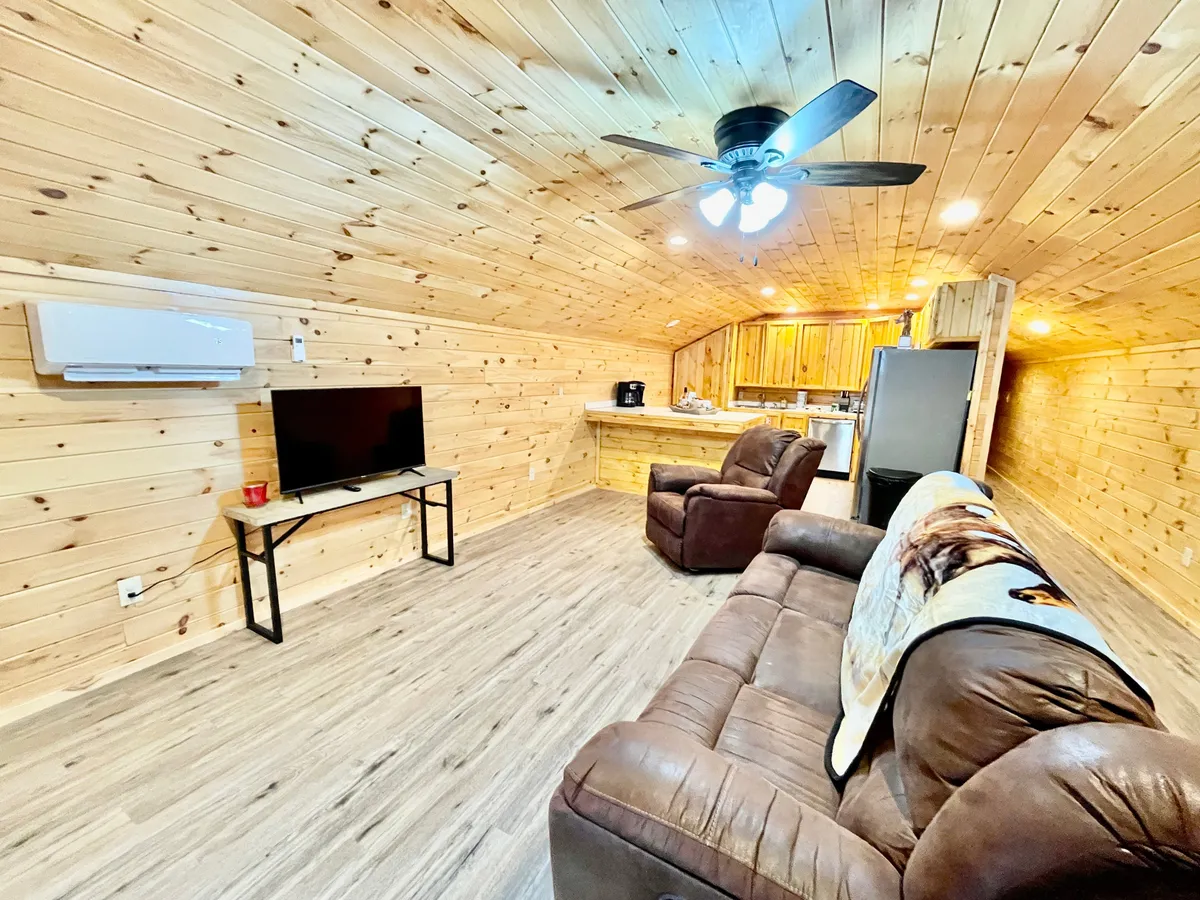 This image showcases a comfortable living area with a plush sofa, a TV, and an open kitchen space in the background. The atmosphere is cozy and inviting, emphasizing a place to unwind after a day on the road. The layout hints at an open-concept design ideal for socializing or relaxing.