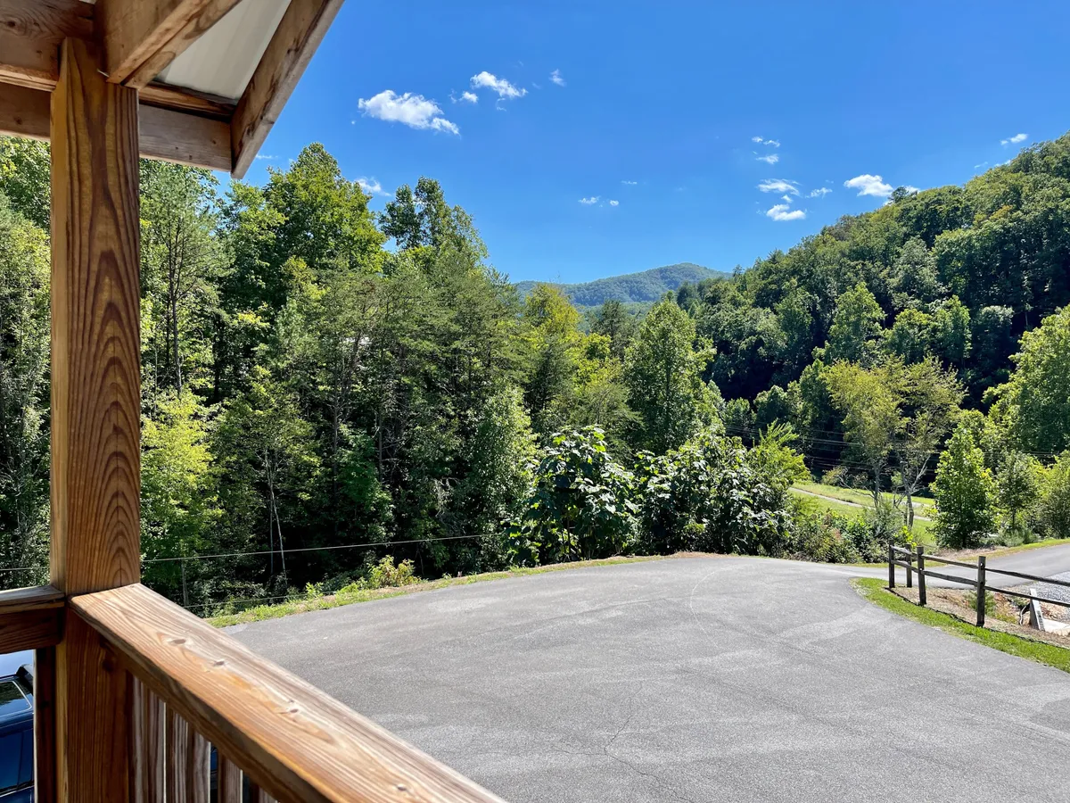 A panoramic view of the mountain landscape showcasing lush greenery and a clear blue sky, evoking a serene and immersive connection to nature. The scene hints at activities like porch relaxation and nature walks.