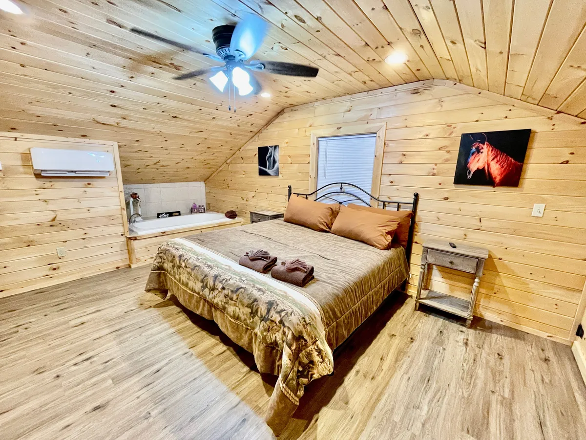A bedroom scene featuring a bed with wooden walls and horse-themed artwork. The window hints at scenic views outside, and the decor reinforces the ranch atmosphere.