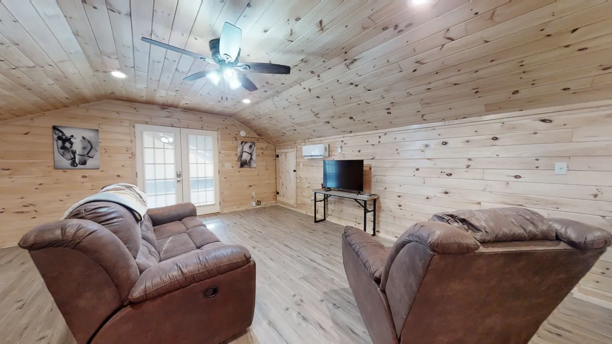 The image presents a cozy living area with plush sofas, a television, warm wooden walls, and double doors that likely lead outside. The arrangement suggests a welcoming space for relaxation and unwinding after a day of exploration.