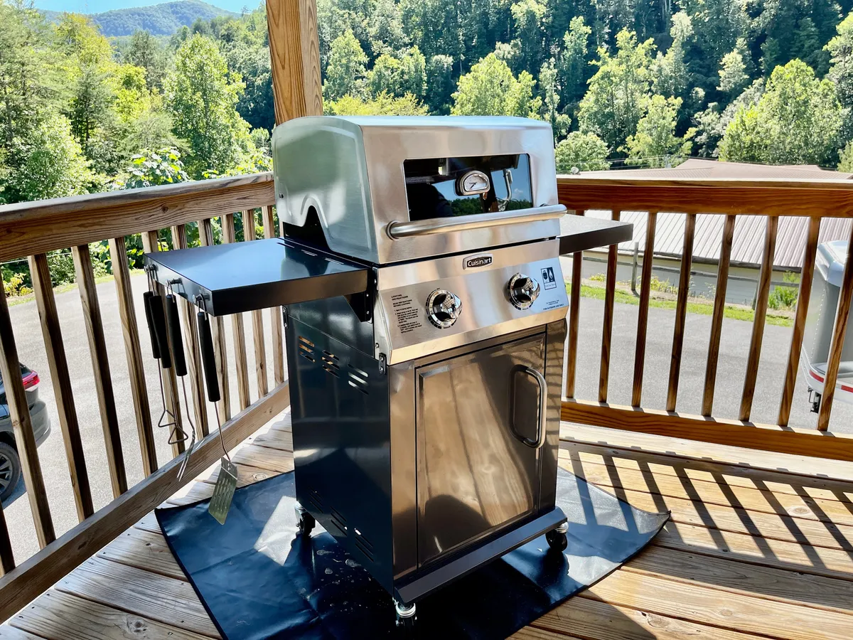 This image showcases an inviting outdoor deck area featuring a grill, sturdy deck railing, and beautiful surrounding nature. The scene evokes the feeling of gathering outdoors, enjoying fresh air, and relaxing in a peaceful rural environment.