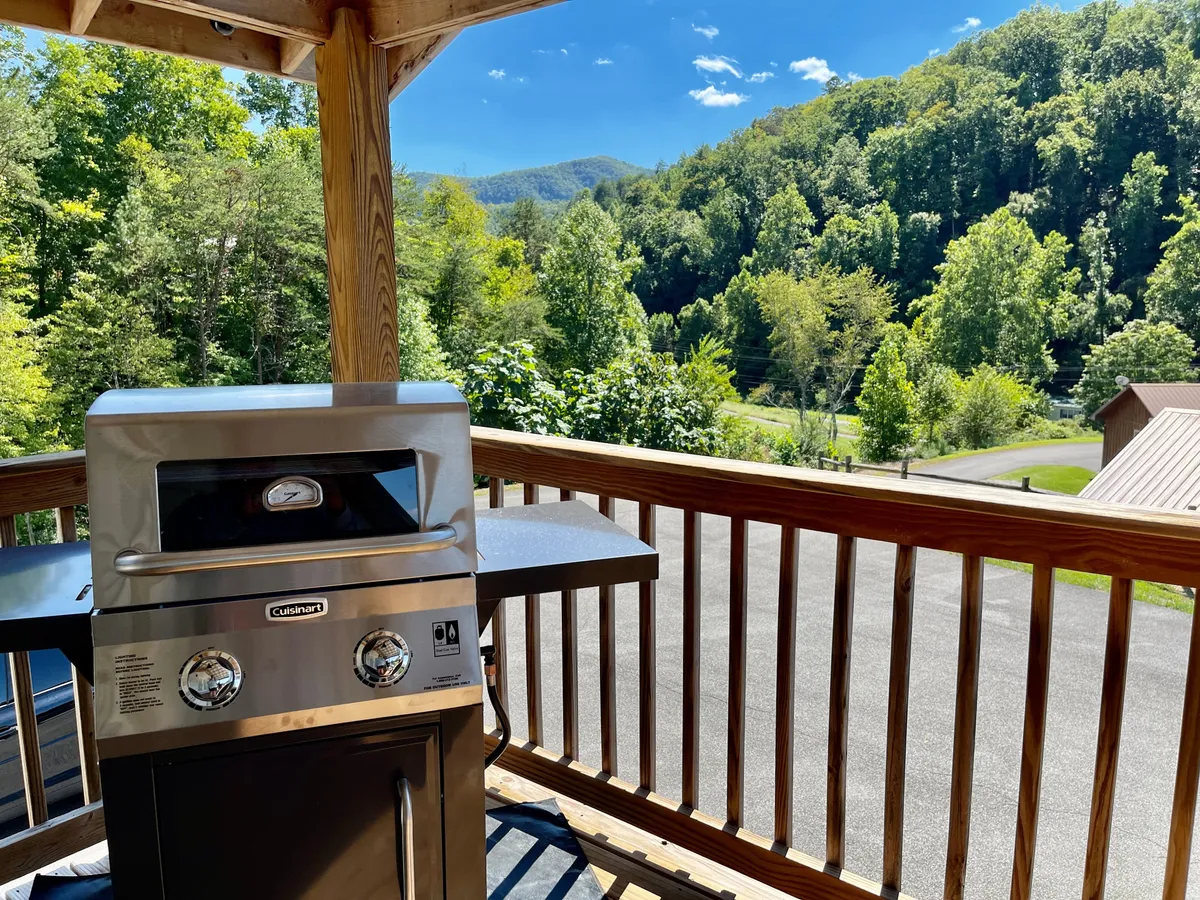 A spacious deck equipped with a grill, overlooking rolling mountains and framed by a classic deck railing. The scene exudes a cheerful mood, suggesting the enjoyment of outdoor dining, sunset watching, and shared experiences in a scenic setting.